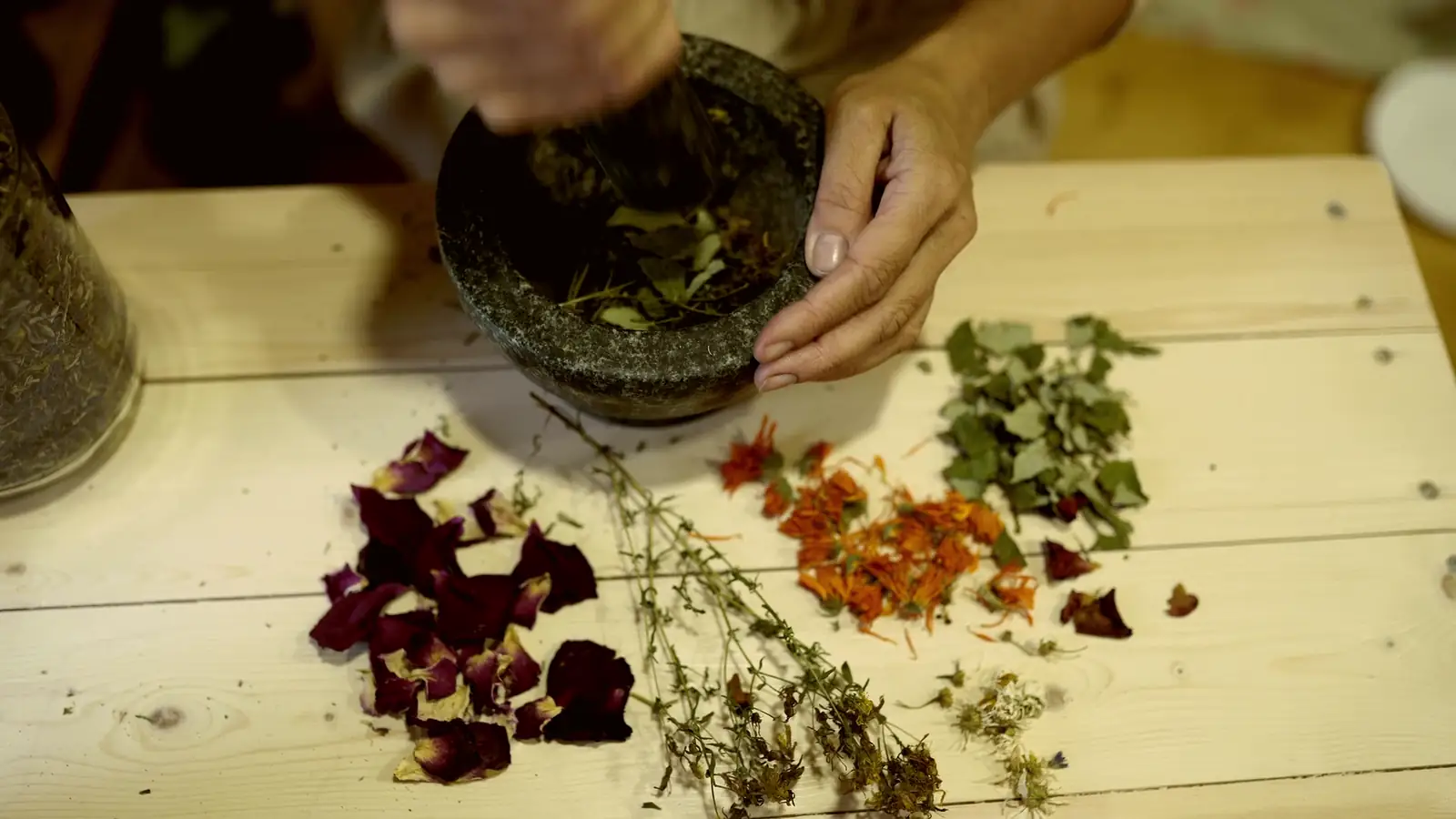 Getrocknete Blüten und Kräuter auf einem Holztisch, daneben ein Steinmörser